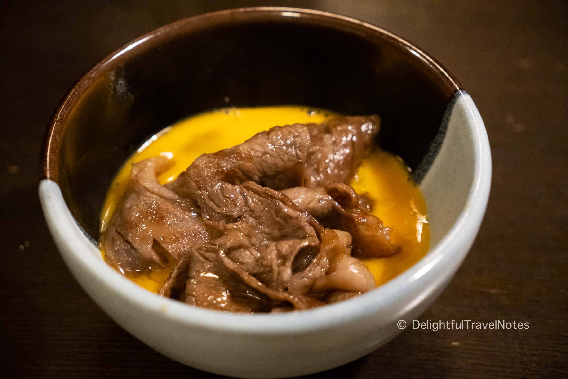 a bowl of cooked sukiyaki beef in beaten egg at Junidanya restaurant in Kyoto.