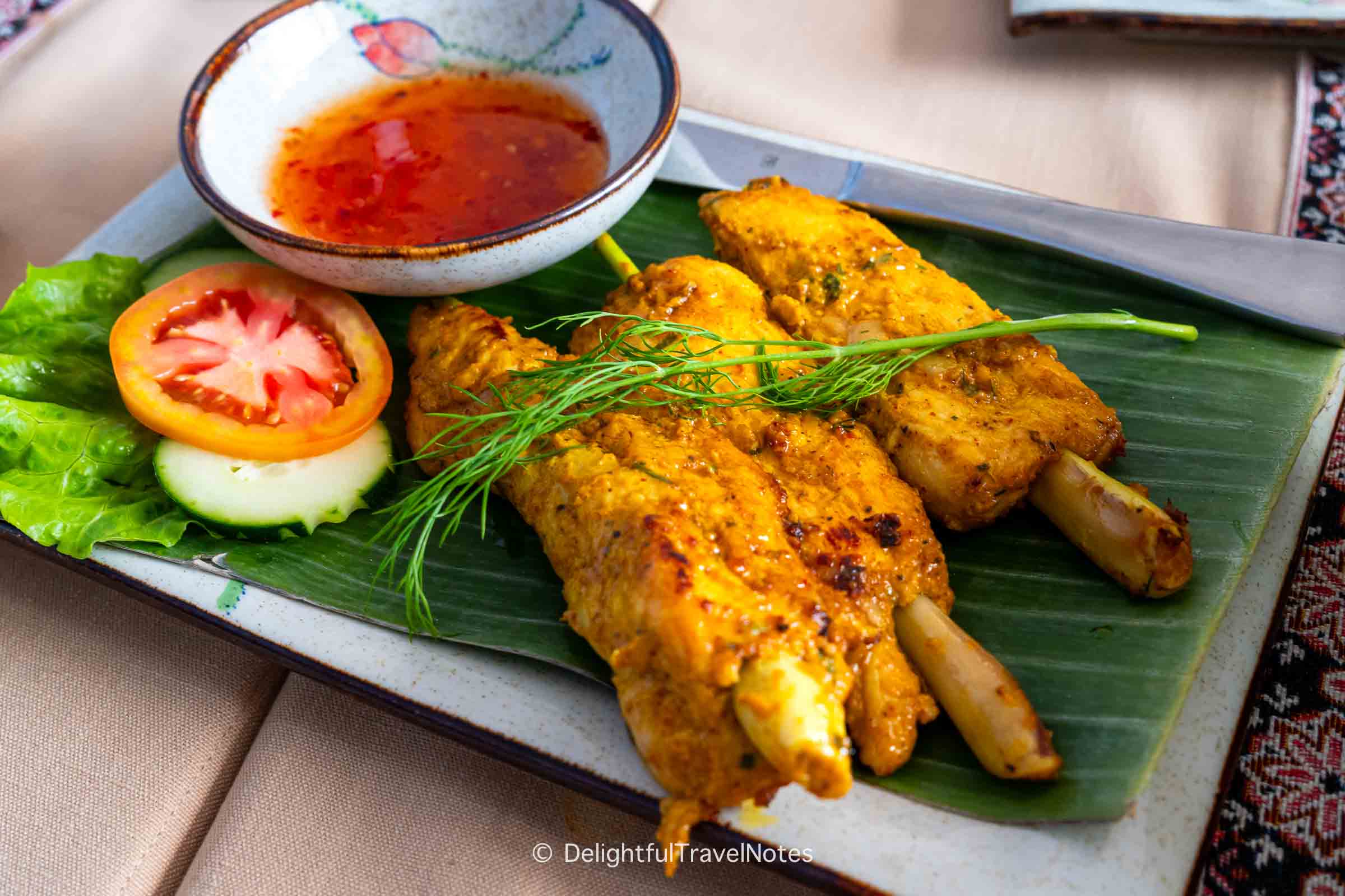 a plate of grilled chicken on lemongrass at Cafe Toui.