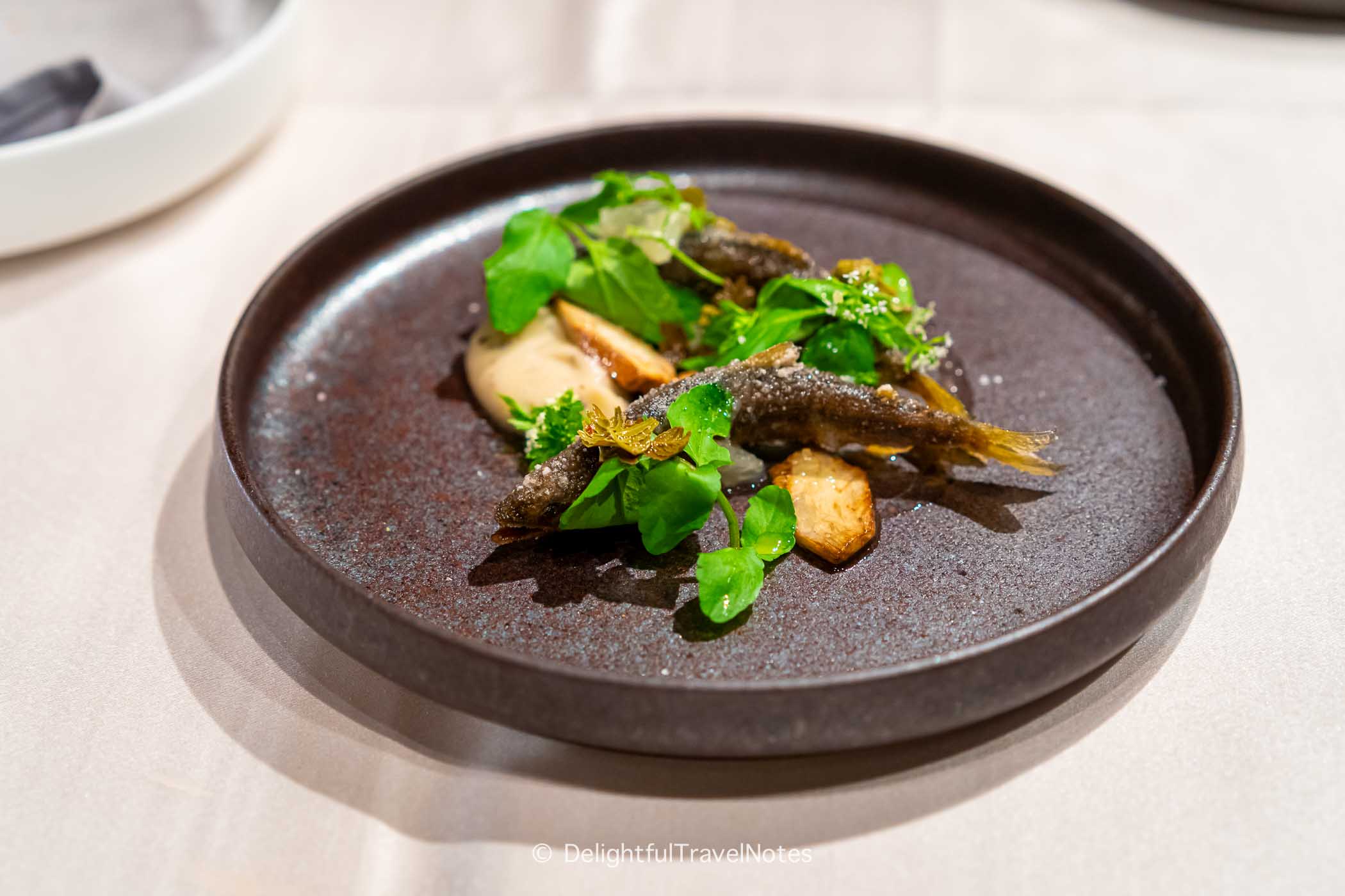 a plate of fried ayu fish with green garnish and sauce.