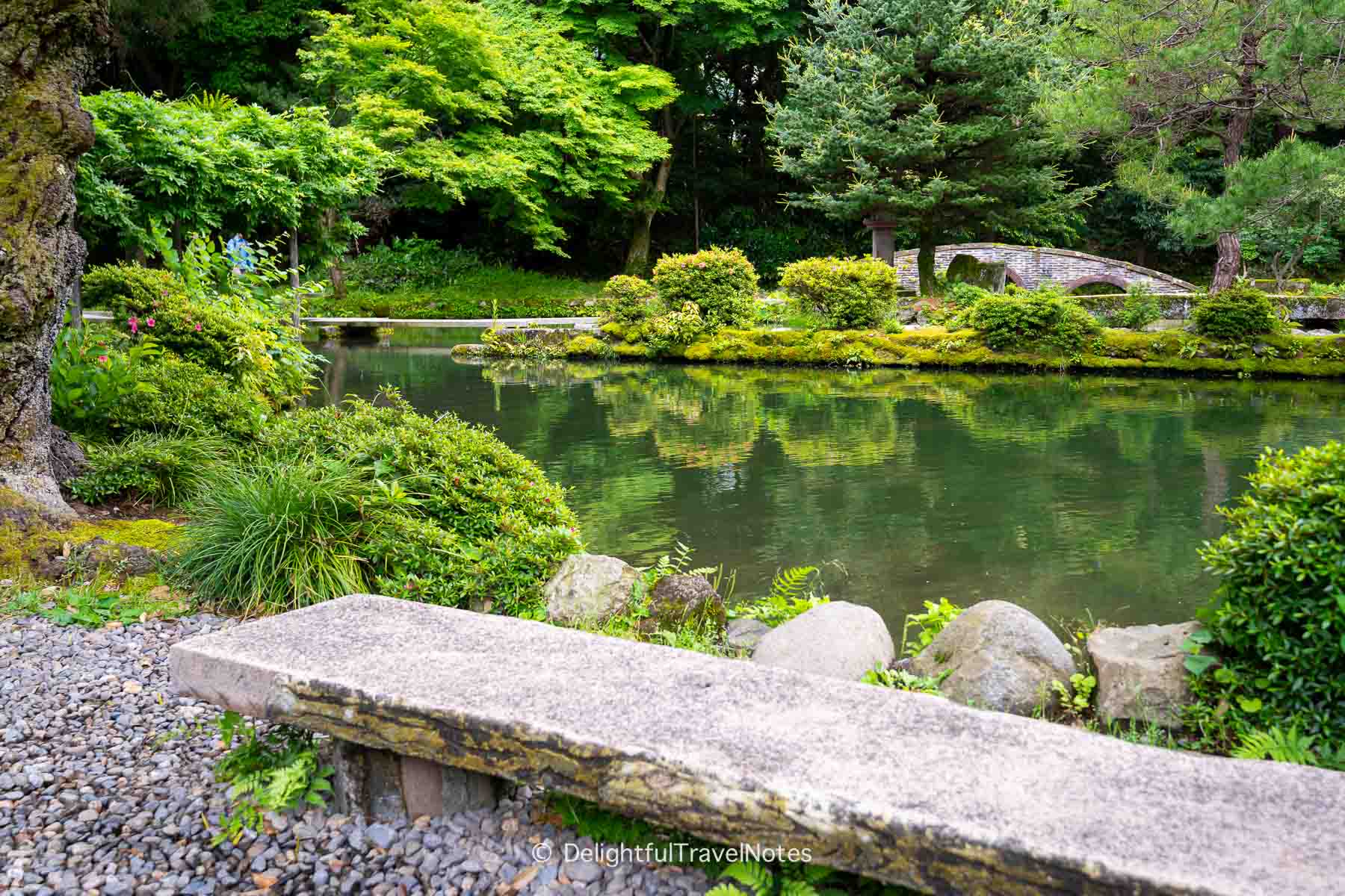 the stone bench at Oyama Shrine in Kanazawa, with the pond and shrubs in the background.