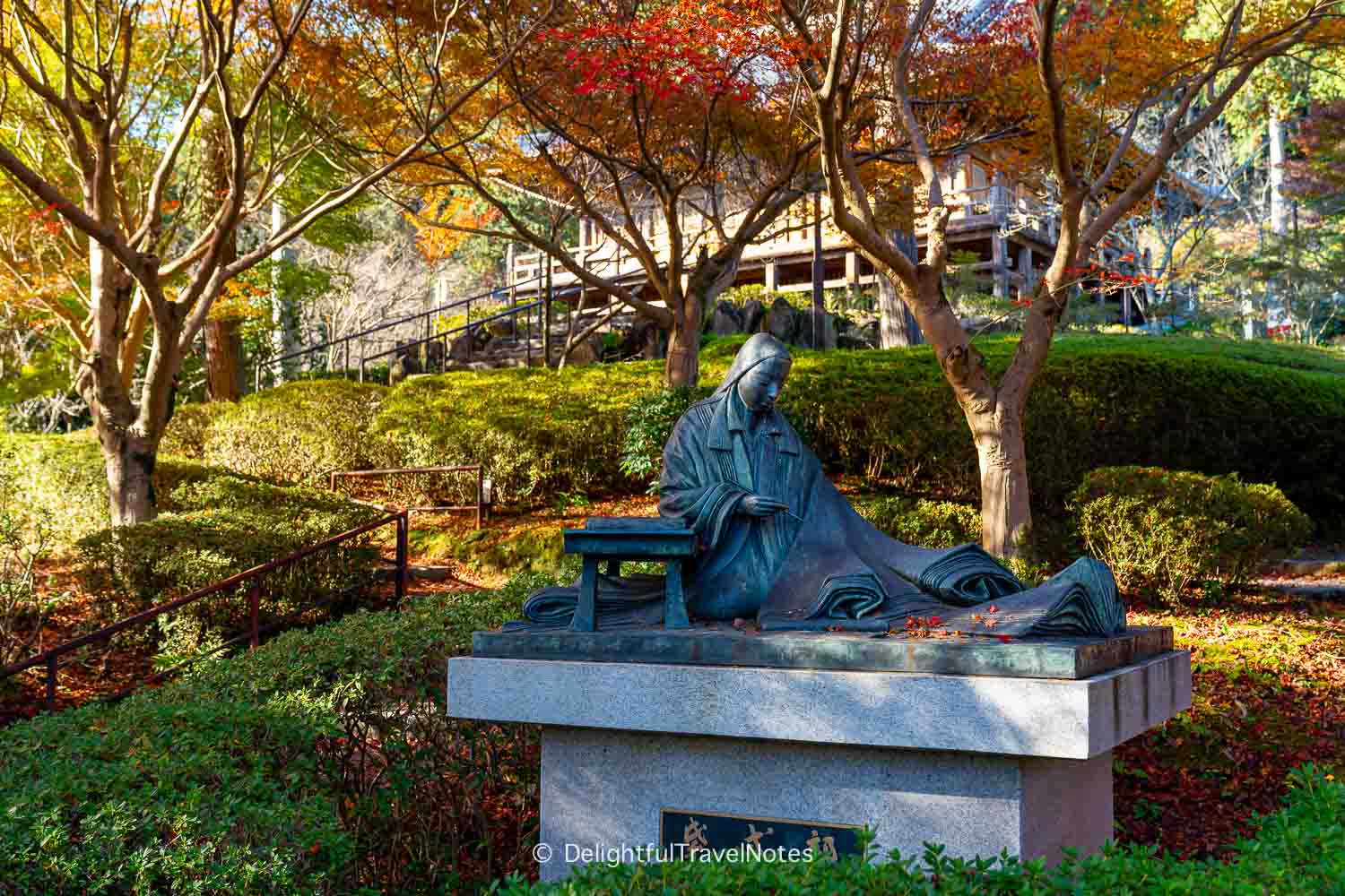 Statue of Murasaki Shikibu under fall foliage on Ishiyamadera temple grounds.